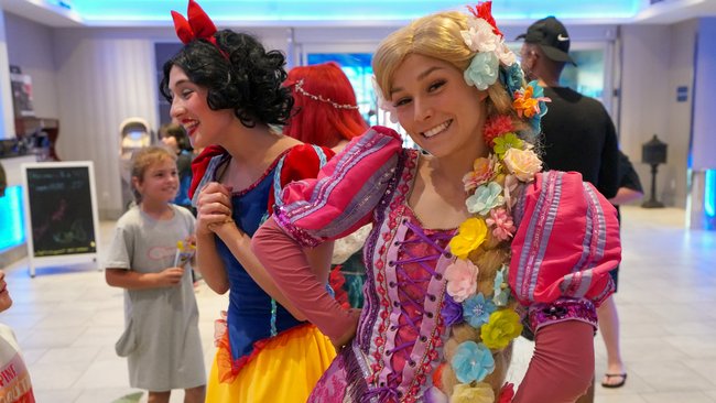 Deux personnages enchanteurs déguisés en princesses de contes de fées interagissent avec des enfants dans le hall de L’Hôtel Québec, créant une ambiance magique et joyeuse.