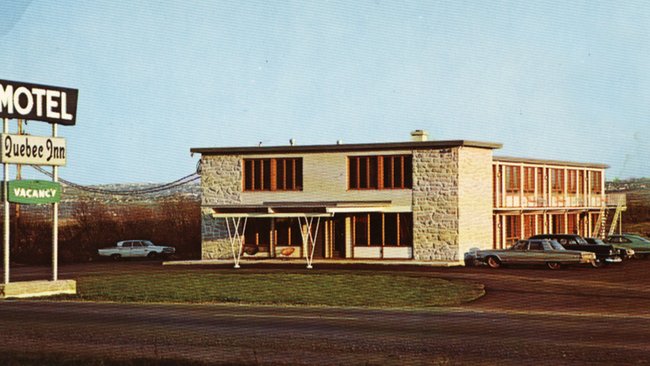 A retro photo of the Quebec Inn motel from the 1970s, showing a stone and wood building surrounded by vintage cars, symbolising the beginnings of Immeubles Jacques Robitaille inc.