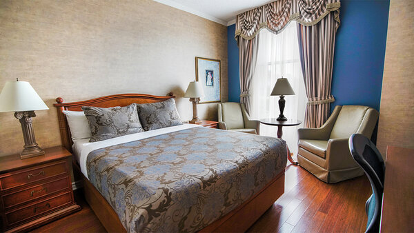 Classic Palace hotel room with king-size bed, armchair and desk, offering a breathtaking view of Quebec City.