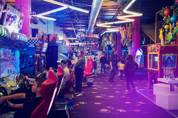 A festive atmosphere is in full swing at the Carie Factory arcade, with children and adults enjoying the bright, colorful games in a vibrant, fun setting.