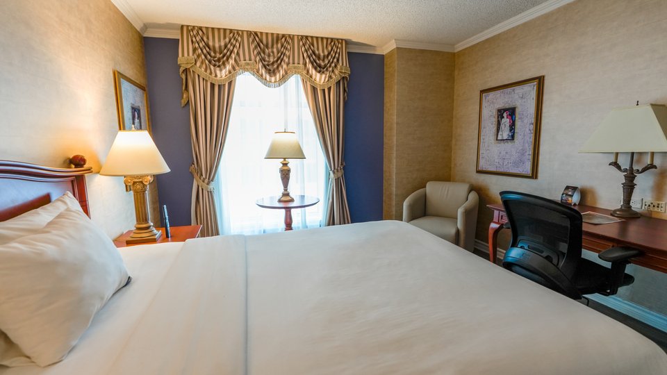 Chambre élégante au Palace Royal Classique, dotée d'un grand lit, d'un bureau et d'une chaise, offrant une vue sur la ville de Québec