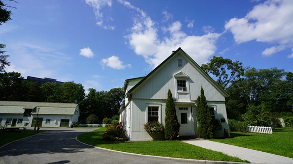 Parc du Bois-de-Coulonge Charmante maison blanche avec un toit vert pointu, entourée d'un jardin soigné et d'arbres majestueux sous un ciel bleu parsemé de nuages au parc du Bois-de-Coulonge, Québec.