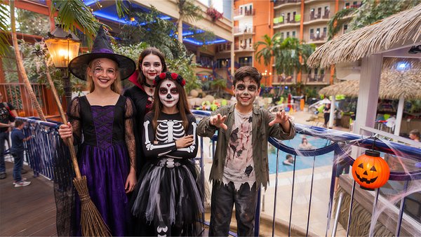 Children dressed up for Halloween pose in front of the indoor pool at L’Hôtel Québec, in a festive atmosphere with Halloween decorations and a glowing pumpkin.