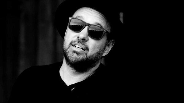 Jonathan Guérette, artiste en prestation musicale à l'Hôtel Palace, portant des lunettes de soleil et un chapeau, capturé dans un portrait en noir et blanc