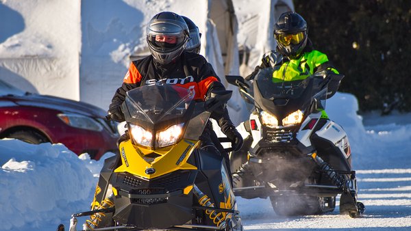 Groupe de motoneigistes devant l'Hôtel Québec Inn par une journée enneigée, avec des motoneiges colorées et des équipements de protection.