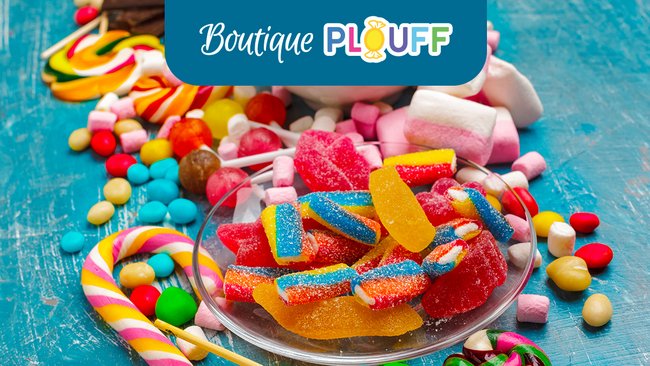  Une variété colorée de bonbons et de sucreries soigneusement disposés sur une table, avec un panneau indiquant "Boutique Plouff" en haut. La Boutique Plouff à L’Hôtel Québec offre une sélection de délices parfaits.