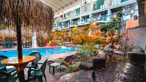 Interior space of Hotel Québec Inn with a pool surrounded by tropical vegetation, tables with straw umbrellas, and balconies overlooking the garden.