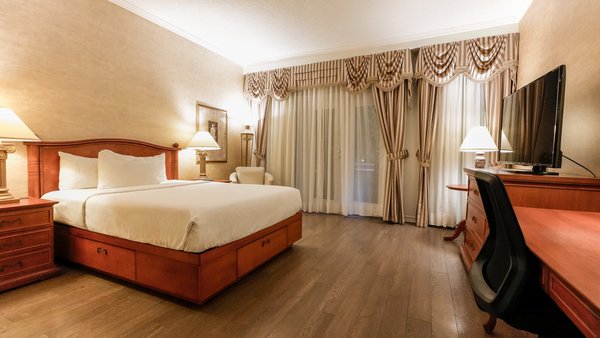 Chambre spacieuse dotée d'un grand lit et d'une télévision, avec une vue partielle sur le jardin du Palace Royal