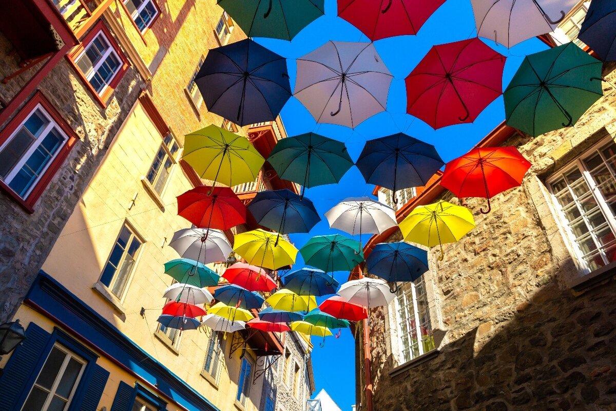 Vieux-Port et le Petit Champlain Installation artistique de parapluies colorés suspendus dans les rues pittoresques du Petit Champlain à Québec, créant une ambiance festive sous un ciel bleu éclatant