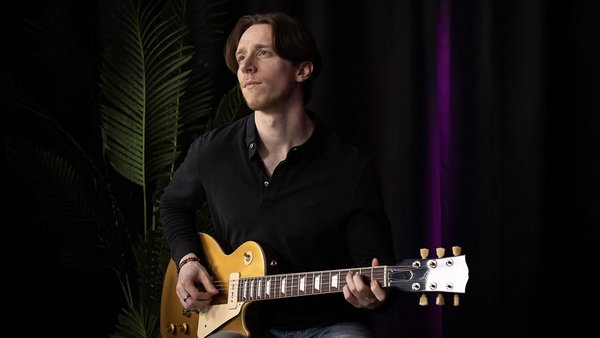 Hugo Benoit, pour une performance musicale intime et captivante dans le jardin tropical de L'Hôtel Québec, avec un décor chaleureux en bois et des lumières douces en arrière-plan.