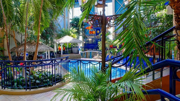Piscine tropicale intérieure de L'Hôtel Québec, avec palmiers et jeux aquatiques. Ambiance de vacances idéale pour la PROMO Réservez Tôt et Économisez JARO.