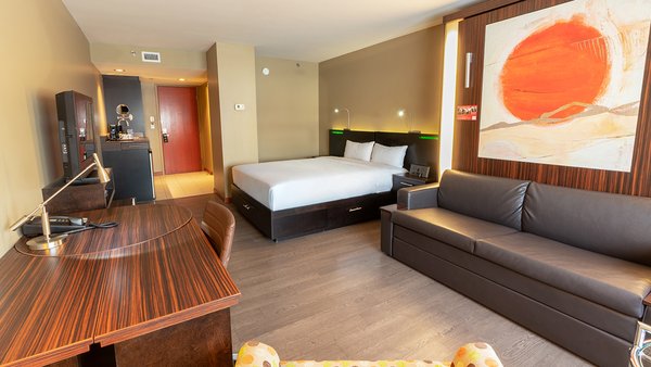 Chambre d'hôtel tendance avec deux grands lits, dont un escamotable transformable en canapé, offrant une ambiance chaleureuse et accueillante à l'Hôtel Must