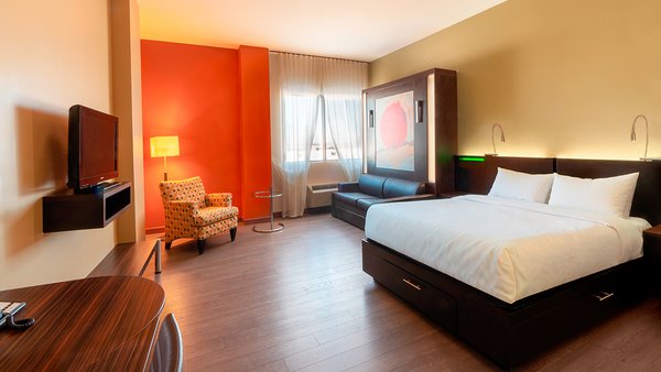 Chambre d'hôtel tendance avec deux grands lits, télévision moderne et foyer chaleureux, offrant confort et convivialité à l'Hôtel Must.