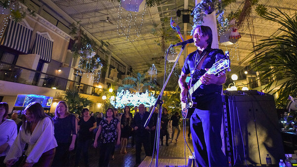 A musical presentation in a tropical garden at the Quebec Inn, featuring singer Remmy Langlois playing guitar, surrounded by a festive, illuminated atmosphere.
