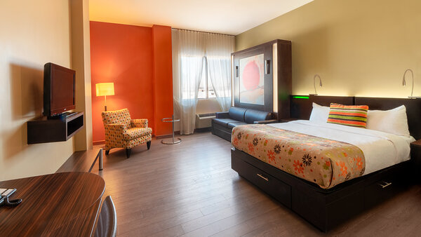Chambre d'hôtel tendance avec deux grands lits, télévision moderne et foyer chaleureux, offrant confort et convivialité à l'Hôtel Must.
