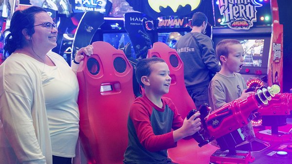 Une famille s'amuse ensemble dans une salle d'arcade lumineuse et colorée, représentant le forfait 'Carie Factory et Hôtel Must