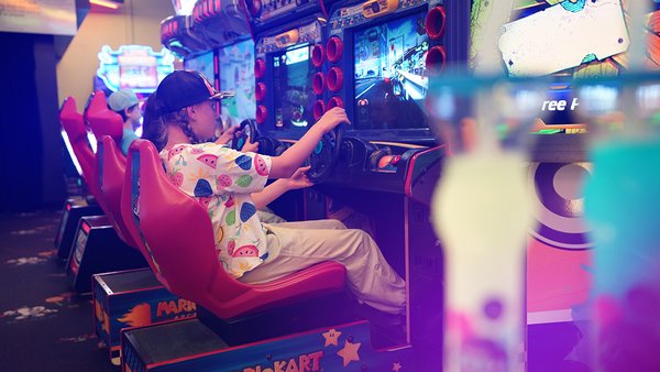 Une famille s'amuse ensemble dans une salle d'arcade lumineuse et colorée, représentant le forfait 'Carie Factory et Hôtel Must