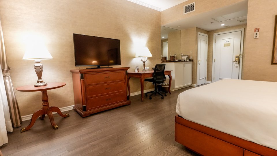 Chambre d'hôtel raffinée avec un grand lit et une télévision, vue partielle sur le jardin du Palace Royal