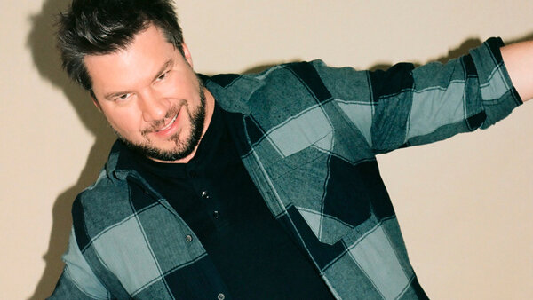 Mark Tebow's musical performance at The Palace Hotel, with a casual style and a plaid shirt, ready to deliver a memorable show.