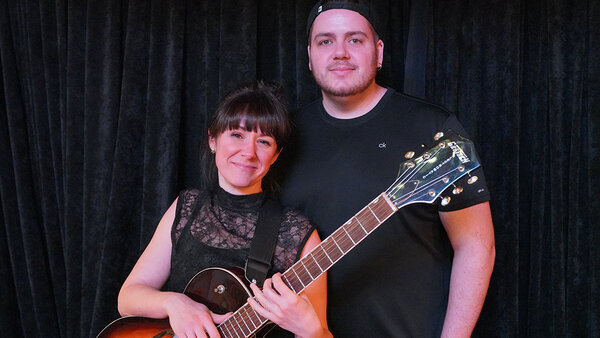 Even en duo lors d'une prestation musicale à l'Hôtel Palace, avec un guitariste et Stéphanie une chanteuse posant devant un rideau noir.