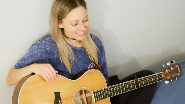 A smiling Maude Carrier, holding an acoustic guitar, during a musical performance at the Hôtel Palace.