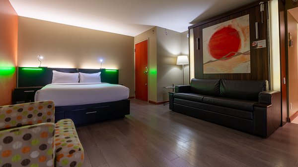 Chambre d'hôtel tendance avec deux grands lits, un bureau, une chaise, et une télévision, sans fenêtre, offrant un espace intime et confortable à l'Hôtel Must.