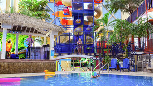 Interior space of Hotel Québec with a pool surrounded by colorful lounge chairs, children's play structures, and tropical decor.