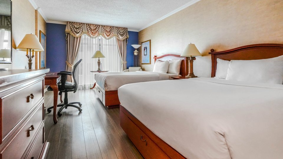 Chambre d'hôtel classique avec deux lits doubles et un bureau, offrant une vue sur l'extérieur du Palace Royal