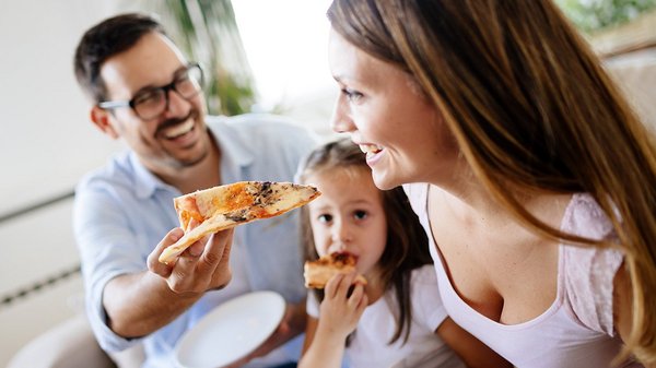 Famille souriante partageant une pizza dans une ambiance conviviale, illustrant le forfait Gourmandise JARO.