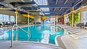 Piscine intérieure de l'Hôtel Must, entourée de grandes plantes en pot, avec un plafond moderne et des espaces de détente lumineux.