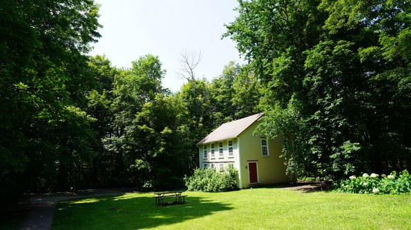 Parc Cartier-Roberval Charmante maison historique avec sa porte rouge, nichée dans une forêt dense, offrant un havre de paix au Parc Cartier-Roberval.
