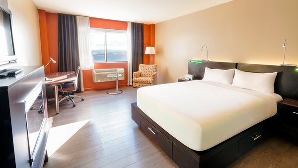 Chambre d'hôtel tendance avec un grand lit, douche multijets, foyer, bureau et télévision, alliant confort moderne et intimité parfaite pour les voyageurs à l'Hôtel Must