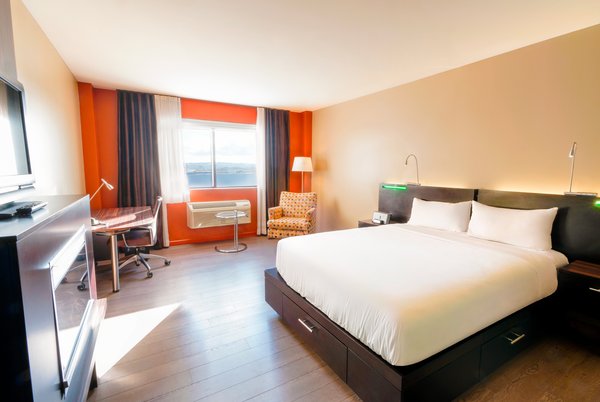 Chambre d'hôtel tendance avec un grand lit, douche multijets, foyer, bureau et télévision, alliant confort moderne et intimité parfaite pour les voyageurs à l'Hôtel Must