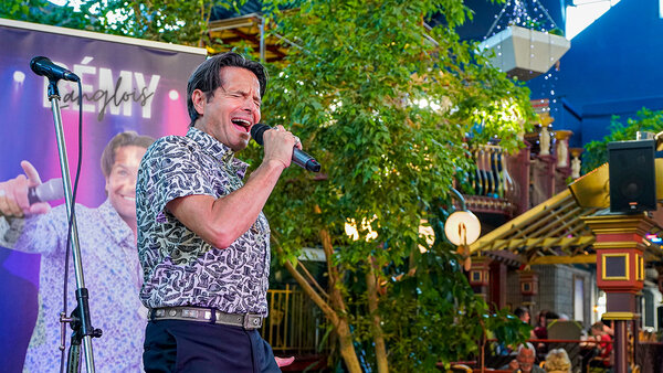 A musical presentation in a tropical garden at the Quebec Inn, featuring singer Remmy Langlois playing guitar, surrounded by a festive, illuminated atmosphere.